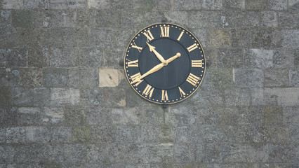 Black clock with gold hands and numerals on stone wall