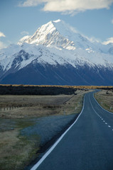 Snow covered Mount Cook with road in the foreground amd blue sky and white clouds, South Island, New Zealand