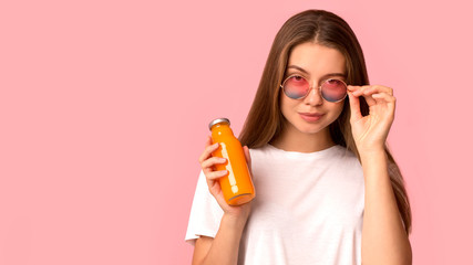Cheerful and cool woman holding orange detox juice on pink