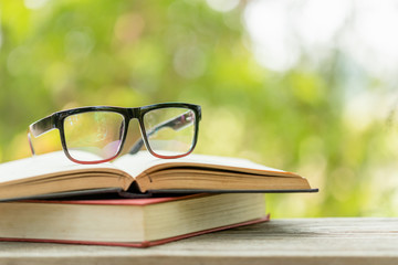 Book and eye glasses on wooden table with abstract green nature blur background. Reading and education concept