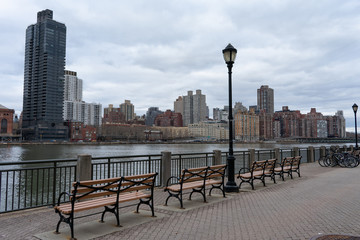 Obraz premium Row of Benches along the East River at Roosevelt Island and looking towards the Upper East Side Skyline of New York City