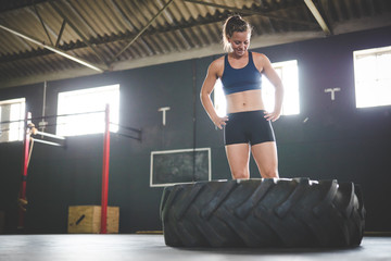 Female fitness model doing cross fit exercise with a massive tyre in a gym