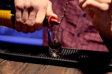 A male bartender makes an alcoholic shot to carefully pour a drink into a glass.