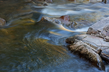 Spring landscape of the Little River rapids captured with motion blur and illuminated with reflections from sunlit foliage and blue sky overhead, Great Smoky Mountains National Park, Tennessee, USA