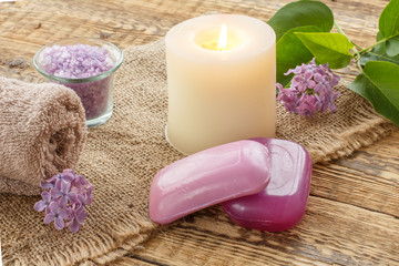 Towel, soap, candle and lilac flowers on wooden background.