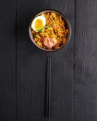 traditional dish of Asian cuisine is a WOK noodle in a clay plate on a black wooden table.