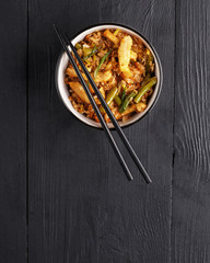 traditional dish of Asian cuisine is a WOK rice in a clay plate on a black wooden table.