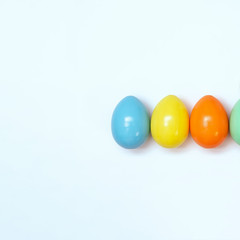 Top view of an Easter composition of painted eggs in bright juicy colors on a white background with a glossy texture. Holiday concept, flat layout, minimalism.