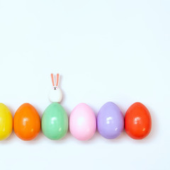 Top view of an Easter composition of painted eggs in bright juicy colors on a white background with a little rabbit. Holiday concept, flat layout, minimalism.