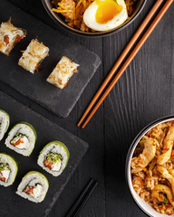 Traditional Asian cuisine sushi rolls and noodles on a black wooden table