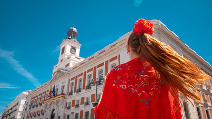 A young caucasian woman chulapa with red flower, traditional dress, and Spanish scarf at Puerta del Sol during San Isidro, the spring festival in May in the downtown of Madrid, the capital of Spain
