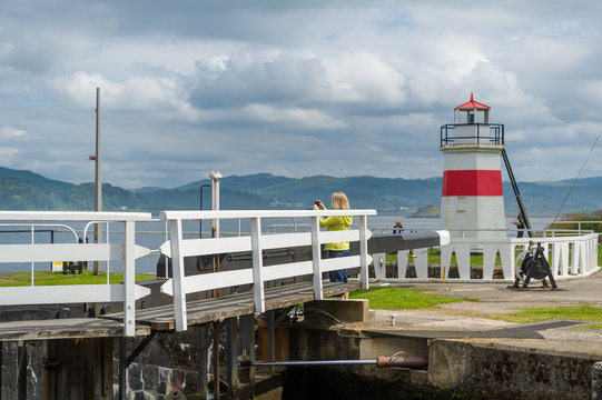 Woman taking pictures at the first bridge of Crinan canal. Sea lighhouse of Crinan. Scotland.