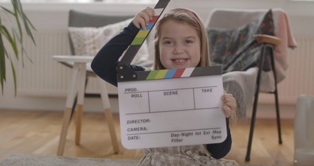 Portrait of a little girl with clapper board on film set in living room