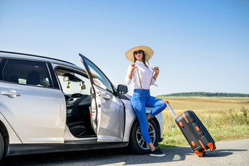 Pretty girl with suitcase standing near car and wiat for her dreaming trip. - obrazy, fototapety, plakaty