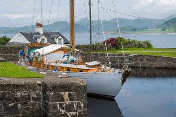 Sailing boat with white hull and old wooden deck and masts docked at Crinan, Scotland.