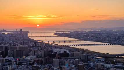 Aerial sunset view of Osaka skyline with the river, round sun, and golden sky as seen from Umeda Sky Building.