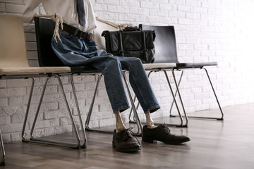 Human skeleton in office wear sitting on chair near brick wall indoors, closeup