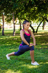 Sports woman doing exercises for stretching the legs, sits on the splits. In the park on the lawn.