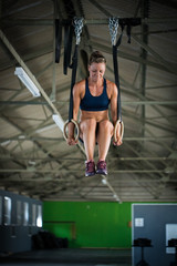 Female fitness model doing cross fit training on over head rings in a gym by pulling herself up