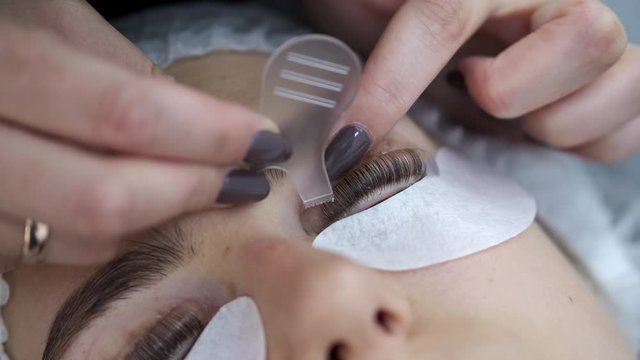 A lash master is doing the eye lashes lamination. The lash maker is brushing the lashes by a lash comb.