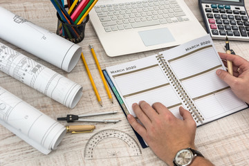 Male hands writing on notepad with part of industrial blueprint with calculator, tools and laptop