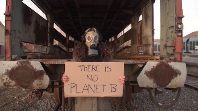 Woman with an antigas mask in an apocalyptic landscape and a banner that says: there is no planet b. Ecological disaster concept