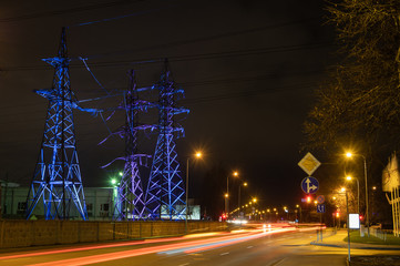 Obraz na płótnie Canvas High voltage towers lightened with blue and violet light in evening with the street lights in foreground, long exposure