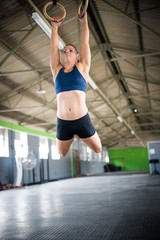 Fototapeta na wymiar Female fitness model doing cross fit training on over head rings in a gym by pulling herself up