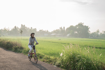 young women wear helmets to ride folding bikes for sports in rice fields background