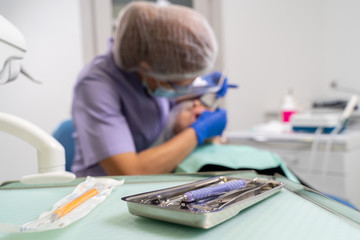 Naklejka premium in the foreground is the focus of dental instruments, in the background is out of focus the dentist is treating the patient.