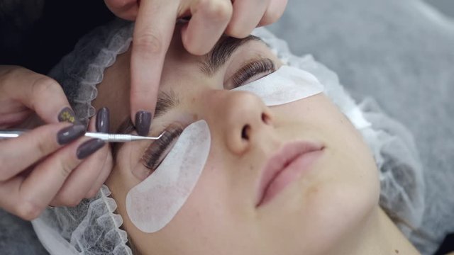 A lash master is fixing the eye lashes on a lift pad. The professional is using a special tool while doing the lamination on both eyes.