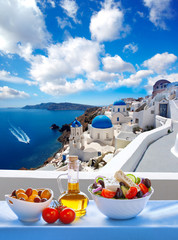 Greek salad against famous church in Oia village, Santorini island in Greece - obrazy, fototapety, plakaty