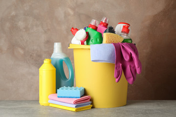 Bottles with detergent and cleaning supplies on brown background, space for text