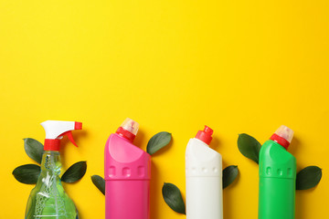 Bottles with detergent and leaves on yellow background, space for text