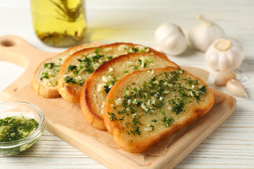 Board with garlic bread on white wooden background, close up