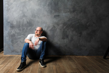 a man sits against the wall. a man in a t-shirt and jeans sits on the floor