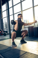 Young muscular caucasian athlete training in gym, doing strength exercises, practicing, work on his upper and lower body, sit-ups with weights. Fitness, wellness, healthy lifestyle concept.