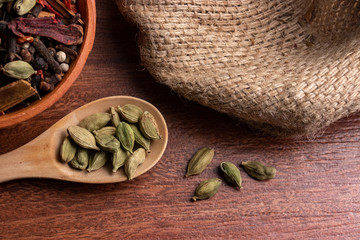 close-up of dried cardamom pods in spoon on wood background, indian spice for cooking