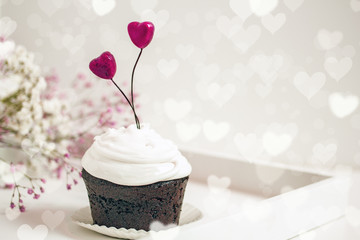 Valentines day cupcake. Cupcake with white cream and red  hearts on a white background, bokeh effect, copy space. St. Valentine's Day card