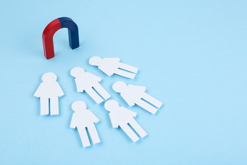 Magnet attracting paper people on light blue background