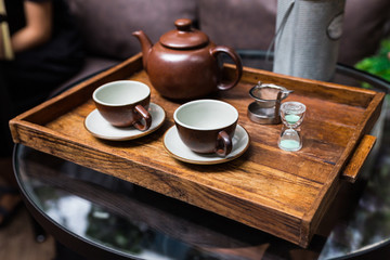 Ceramic vintage cups, mug and small sand clock, equipment for making dry flower with tea stainless steel tea strainer infuser in wooden tray.