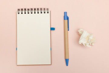 Crumpled paper ball, pen and notebook with space for text on a beige pastel background. No inspiration for writing. View from above.