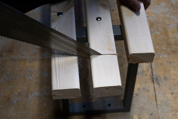 Sawing or cutting a wooden board or bar with a hand saw or hacksaw during carpentry or carpentry work at a construction site.