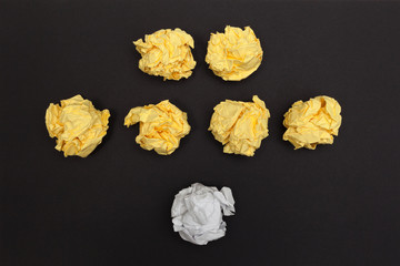 Crumpled white ball speaking to an audience yellow balls on a black paper background. Office life concept. Top view.