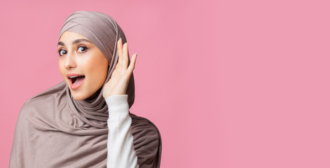 Curious muslim girl in hijab eavesdropping with hand near ear
