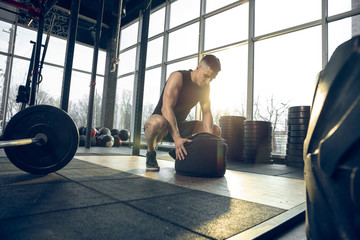 Control. Young muscular caucasian athlete training in gym, doing strength exercises, practicing, work on his upper body with weights and ball. Fitness, wellness, sport, healthy lifestyle concept.