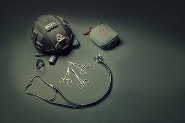 First aid kit, phonendoscope, a set of scissors with a helmet lie on a green background. View to...