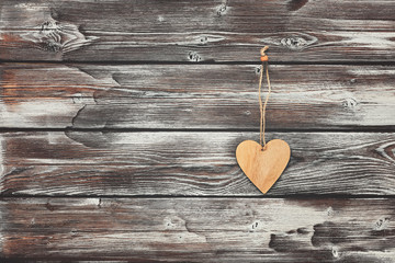 A wooden heart hangs on an old dark shabby wall from wooden boards. Greeting card. Copy space.