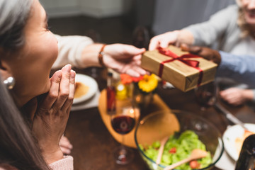 cropped view of woman looking at her multicultural friends holding gift during dinner