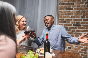 cropped view of woman clinking with smiling multicultural friends during dinner